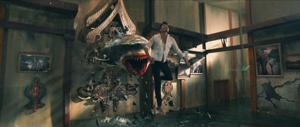 Screenshot aus dem Film "Shark Escape": Ein Mann und ein digital animierter Hai springen durch ein Loch in einer Wand in die überschwemmte Lobby eines Hotels.