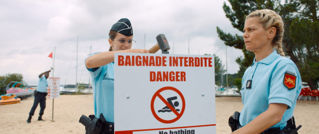 Drei Personen in französischen Polizeiuniformen stellen Warnschilder an einem Strand auf.