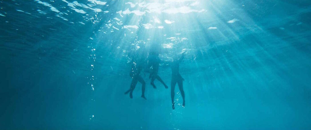 Eine Unterwasseraufnahme von vier in einiger Entfernung schwimmenden Menschen.