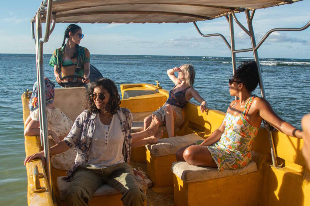 Fünf Frauen in sommerlicher Kleidung sitzen auf einem kleinen, gelben Motorboot und fahren übers Meer.