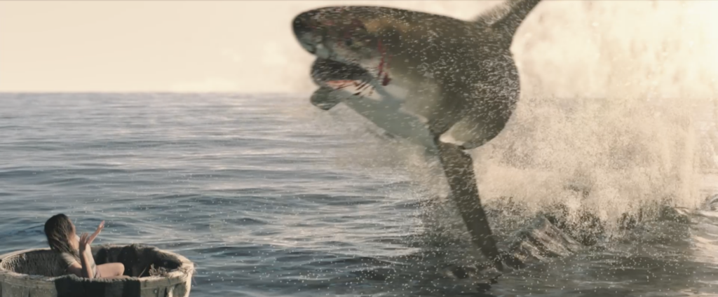 Eine Person treibt unten links im Bild in einer Wann im Meer. Das Bild wird von einem riesigen, CGI-erzeugten Hai dominiert, der vor ihr aus dem Wasser springt. Copyright: Leonine Distribution